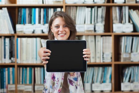simsearch:400-07141917,k - Portrait of a happy female student against bookshelf holding out tablet PC in the library Stock Photo - Budget Royalty-Free & Subscription, Code: 400-07142731