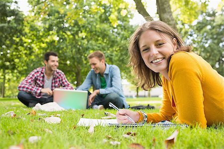 simsearch:632-05816947,k - Portrait of a smiling female writing notes with two students using laptop in background at the park Foto de stock - Super Valor sin royalties y Suscripción, Código: 400-07143567