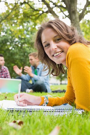 simsearch:632-05816947,k - Portrait of a smiling female writing notes with two students using laptop in background at the park Foto de stock - Super Valor sin royalties y Suscripción, Código: 400-07143568