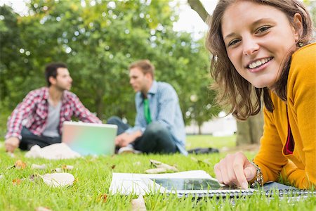 simsearch:632-05816947,k - Portrait of a young student using tablet PC while two males using laptop in background at the park Photographie de stock - Aubaine LD & Abonnement, Code: 400-07143573