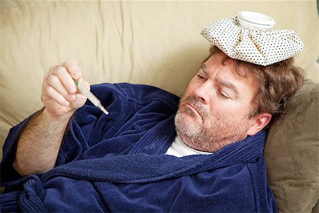 sick ice pack - Man in his bathrobe on the couch, home sick from work.  He has an icepack on his head and is taking his temperature. Stock Photo - Budget Royalty-Free & Subscription, Code: 400-07168197