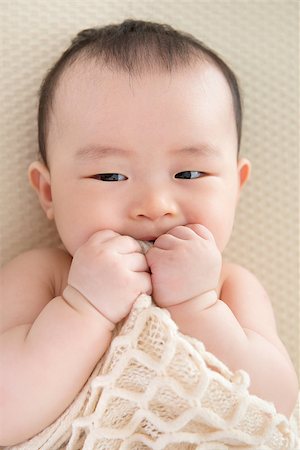simsearch:400-07173561,k - Adorable six months old teething Asian baby girl lying on bed biting blanket. Foto de stock - Royalty-Free Super Valor e Assinatura, Número: 400-07168921
