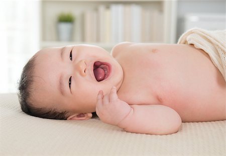 simsearch:400-07173561,k - Happy six months old Asian baby girl lying on bed laughing. Foto de stock - Royalty-Free Super Valor e Assinatura, Número: 400-07168934