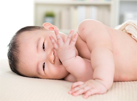 simsearch:400-07173561,k - Adorable six months old Asian baby girl lying on bed biting fingers. Foto de stock - Royalty-Free Super Valor e Assinatura, Número: 400-07168933