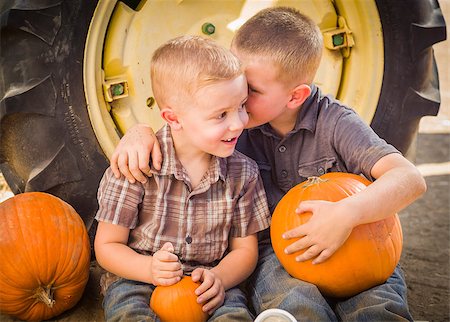 simsearch:400-07173780,k - Two Boys Sitting Against a Tractor Tire Holding Pumpkins and Whispering Secrets in Rustic Setting. Stockbilder - Microstock & Abonnement, Bildnummer: 400-07174826