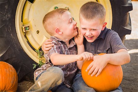 simsearch:400-07179959,k - Two Boys Sitting Against a Tractor Tire Holding Pumpkins and Whispering Secrets in Rustic Setting. Stockbilder - Microstock & Abonnement, Bildnummer: 400-07174827