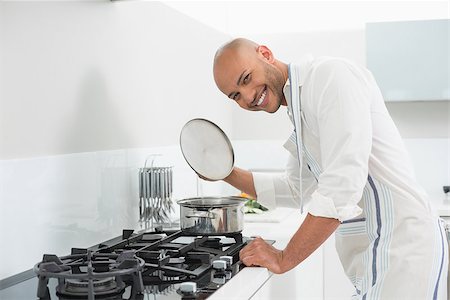 simsearch:400-07177497,k - Side view of a smiling young man preparing food in the kitchen at home Foto de stock - Super Valor sin royalties y Suscripción, Código: 400-07177487