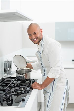 simsearch:400-07177497,k - Side view of a smiling young man preparing food in the kitchen at home Foto de stock - Super Valor sin royalties y Suscripción, Código: 400-07177490