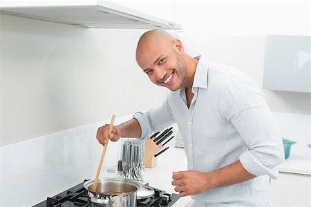 simsearch:400-07177497,k - Side view of a smiling young man preparing food in the kitchen at home Foto de stock - Super Valor sin royalties y Suscripción, Código: 400-07177535
