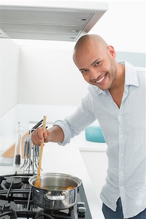 simsearch:400-07177497,k - Side view of a smiling young man preparing food in the kitchen at home Foto de stock - Super Valor sin royalties y Suscripción, Código: 400-07177536