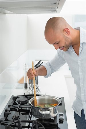 simsearch:400-07177497,k - Side view of a smiling young man preparing food in the kitchen at home Foto de stock - Super Valor sin royalties y Suscripción, Código: 400-07177537