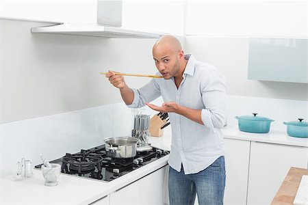 simsearch:400-07177497,k - Portrait of a young man tasting food while preparing in the kitchen at home Foto de stock - Super Valor sin royalties y Suscripción, Código: 400-07177538