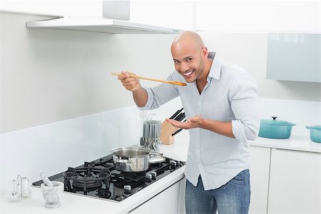 simsearch:400-07177497,k - Portrait of a smiling young man tasting food while preparing in the kitchen at home Foto de stock - Super Valor sin royalties y Suscripción, Código: 400-07177539
