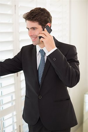 Smiling young businessman peeking through blinds while on call in office Stock Photo - Budget Royalty-Free & Subscription, Code: 400-07177858