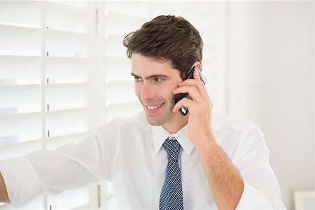 Smiling young businessman peeking through blinds while on call in office Stock Photo - Budget Royalty-Free & Subscription, Code: 400-07177868