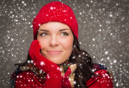 snow cosy - Happy Mixed Race Woman Wearing Winter Hat and Gloves Enjoys Watching the Snow Fall Looking to the Side on Gray Background. Stock Photo - Budget Royalty-Free & Subscription, Code: 400-07179037