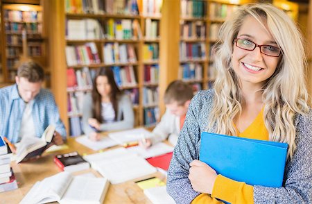 simsearch:400-07180633,k - Portrait of a smiling female student with others in background in the college library Foto de stock - Super Valor sin royalties y Suscripción, Código: 400-07180656