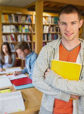 simsearch:400-07180633,k - Portrait of a smiling male student with others in background in the college library Foto de stock - Super Valor sin royalties y Suscripción, Código: 400-07180652