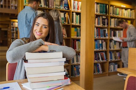 simsearch:400-07180633,k - Portrait of a smiling female student with stack of books while others in background at the college library Foto de stock - Super Valor sin royalties y Suscripción, Código: 400-07180666