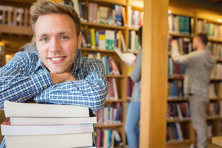 simsearch:400-07180633,k - Portrait of a smiling male student with stack of books while others in background at the college library Foto de stock - Super Valor sin royalties y Suscripción, Código: 400-07180667