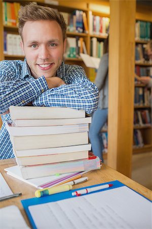 Portrait of a smiling male student with stack of books while others in background at the college library Stock Photo - Budget Royalty-Free & Subscription, Code: 400-07180668