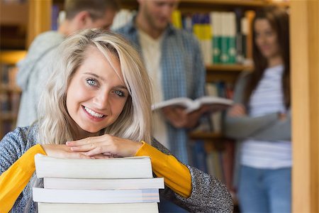 simsearch:400-07180633,k - Portrait of a smiling female student with stack of books while others in background at the college library Foto de stock - Super Valor sin royalties y Suscripción, Código: 400-07180670