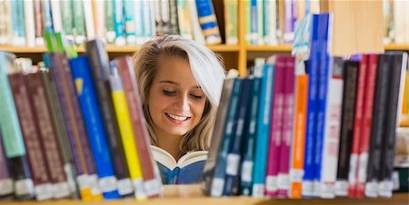 simsearch:400-07141917,k - Smiling young female student reading book amid bookshelves in the college library Stock Photo - Budget Royalty-Free & Subscription, Code: 400-07180751