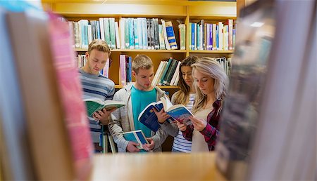 simsearch:400-07180633,k - Group of four students reading book against bookshelf in the college library Foto de stock - Super Valor sin royalties y Suscripción, Código: 400-07180784