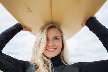 Close up of a smiling young woman in wet suit holding surfboard over head at beach Stock Photo - Budget Royalty-Free & Subscription, Code: 400-07180993