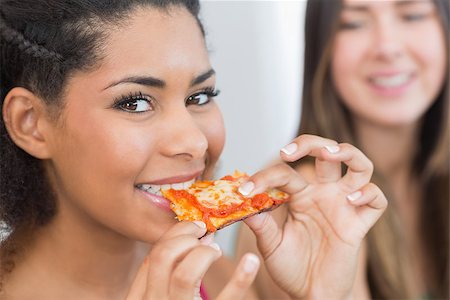 simsearch:400-07181183,k - Close up portrait of a young female eating pizza with blurred friend at home Photographie de stock - Aubaine LD & Abonnement, Code: 400-07181185