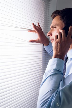 Side view of a young businessman peeking through blinds while on call in office Stock Photo - Budget Royalty-Free & Subscription, Code: 400-07181488