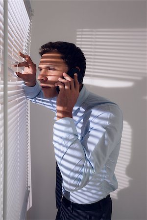 simsearch:400-07266908,k - Side view of a young businessman peeking through blinds while on call in office Photographie de stock - Aubaine LD & Abonnement, Code: 400-07181498