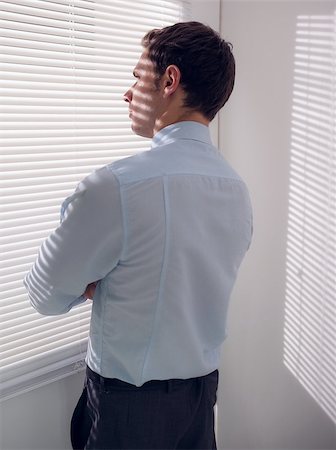 simsearch:400-07266908,k - Rear view of a young businessman peeking through blinds in office Photographie de stock - Aubaine LD & Abonnement, Code: 400-07181509