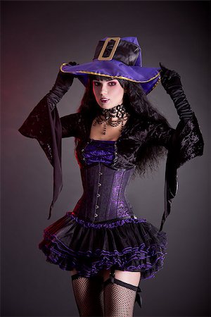 simsearch:400-07209173,k - Smiling witch in purple and black gothic Halloween costume, studio shot on black background Fotografie stock - Microstock e Abbonamento, Codice: 400-07210681
