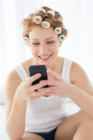 Relaxed young woman in hair curlers text messaging while sitting on bed at home Stock Photo - Budget Royalty-Free & Subscription, Code: 400-07227960