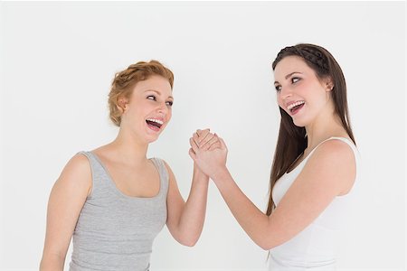 Two cheerful young female friends arm wrestling against white background Stock Photo - Budget Royalty-Free & Subscription, Code: 400-07228280