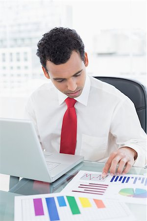 simsearch:400-07931035,k - Serious young businessman with laptop working on graphs at office desk Stock Photo - Budget Royalty-Free & Subscription, Code: 400-07228489