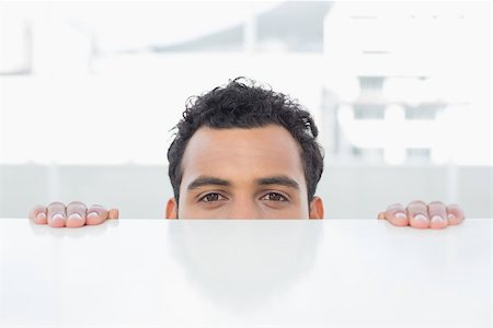 Close-up portrait of a young businessman peeking behind the desk at bright office Stock Photo - Budget Royalty-Free & Subscription, Code: 400-07228526