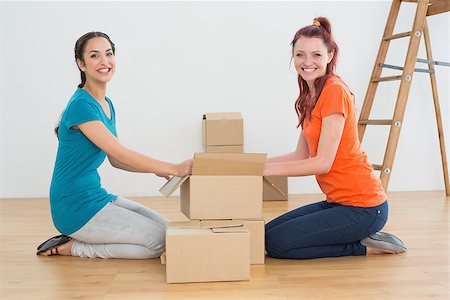 Side view portrait of two happy friends moving together in a new house and unwrapping boxes Stock Photo - Budget Royalty-Free & Subscription, Code: 400-07229376