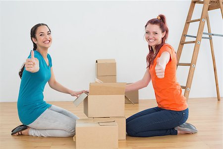 Portrait of two happy female friends gesturing thumbs up with boxes in a new house Stock Photo - Budget Royalty-Free & Subscription, Code: 400-07229377