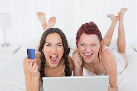 simsearch:6109-06194946,k - Portrait of cheerful young female friends doing online shopping through laptop and credit card in bed Fotografie stock - Microstock e Abbonamento, Codice: 400-07229583