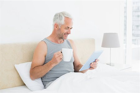 simsearch:400-07230809,k - Side view of a smiling mature man with digital tablet and coffee table sitting in bed at home Foto de stock - Super Valor sin royalties y Suscripción, Código: 400-07230665