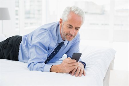 sophisticated home smile - Smiling relaxed well dressed man text messaging in bed at home Stock Photo - Budget Royalty-Free & Subscription, Code: 400-07230739
