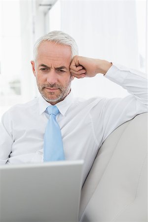 simsearch:400-07230809,k - Concentrated mature businessman using laptop on sofa in living room at home Foto de stock - Super Valor sin royalties y Suscripción, Código: 400-07230777