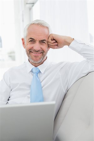 sophisticated home smile - Portrait of a smiling mature businessman using laptop on sofa in living room at home Stock Photo - Budget Royalty-Free & Subscription, Code: 400-07230778