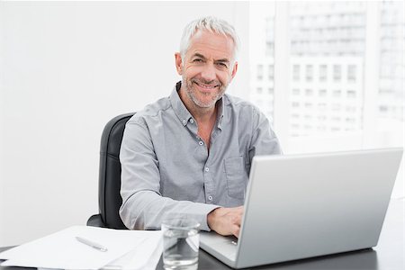 simsearch:400-07230809,k - Portrait of a smiling mature businessman using laptop at desk in a bright office Foto de stock - Super Valor sin royalties y Suscripción, Código: 400-07230824