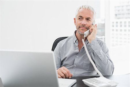 simsearch:400-07230809,k - Serious mature businessman on call in front of laptop at desk in a bright office Foto de stock - Super Valor sin royalties y Suscripción, Código: 400-07230827