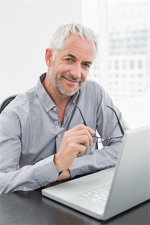 simsearch:400-07230809,k - Portrait of a smiling mature businessman using laptop at desk in a bright office Foto de stock - Super Valor sin royalties y Suscripción, Código: 400-07230822