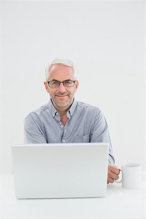 simsearch:400-07230809,k - Portrait of a smiling mature businessman with laptop and coffee cup against white background Foto de stock - Super Valor sin royalties y Suscripción, Código: 400-07230831