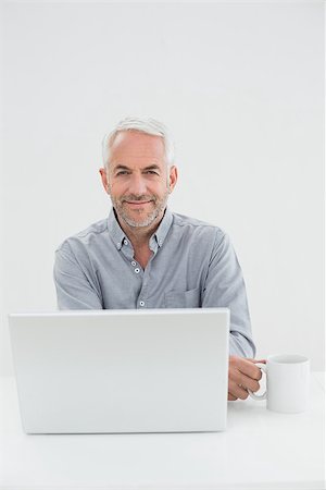 simsearch:400-07230809,k - Portrait of a smiling mature businessman with laptop and coffee cup against white background Foto de stock - Super Valor sin royalties y Suscripción, Código: 400-07230832